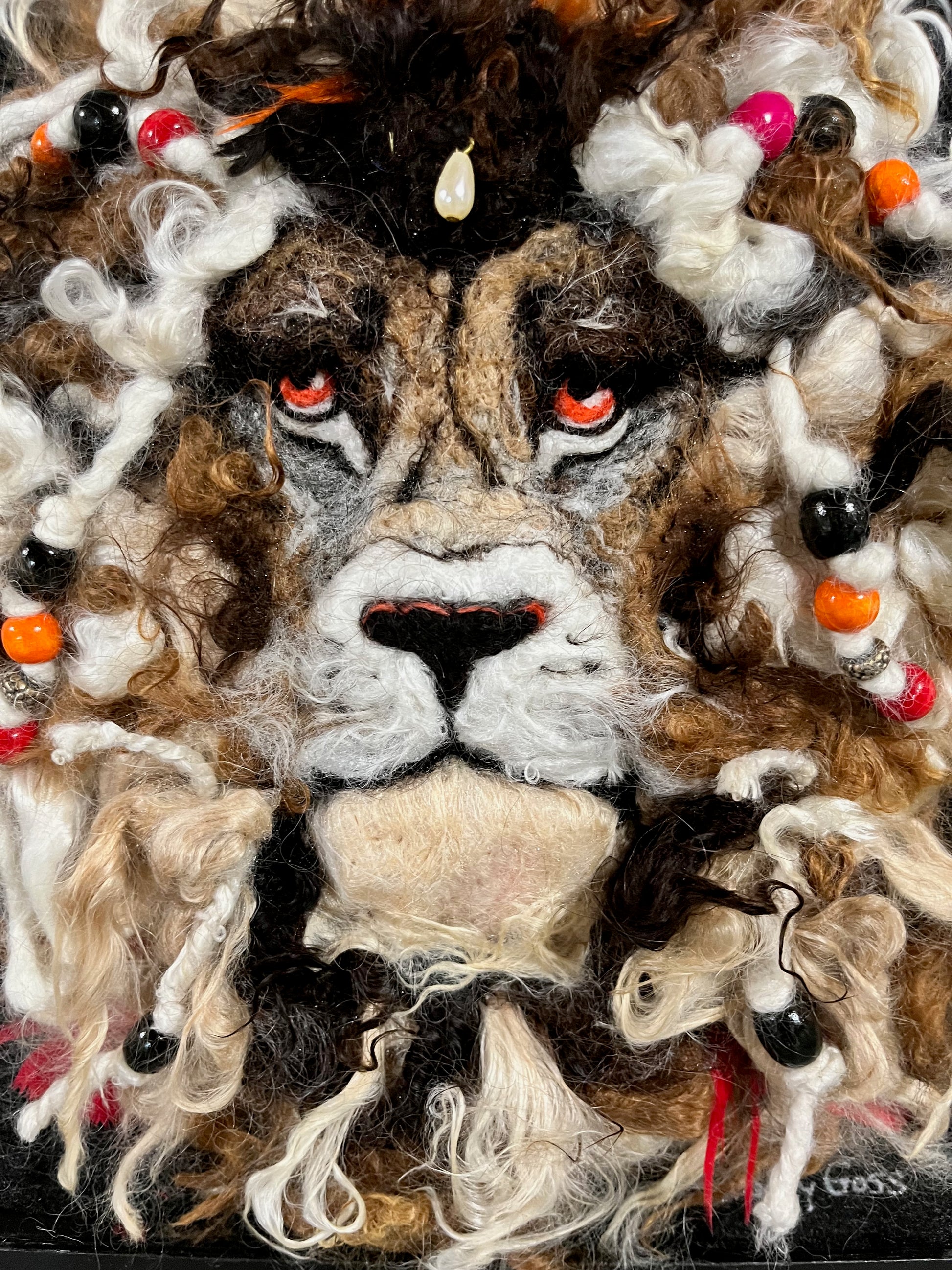 Close-up of a textured lion's face with colorful beads and fibers.